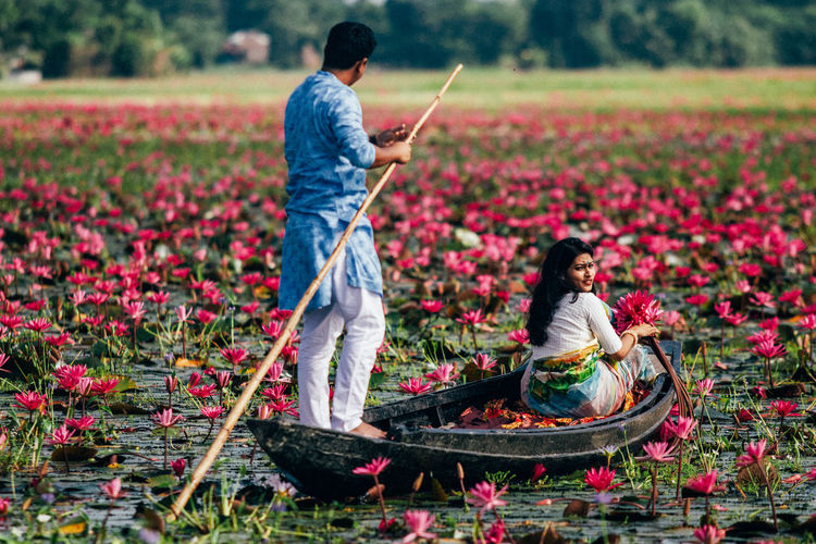Rear view of man with arms outstretched standing on waterlily pond