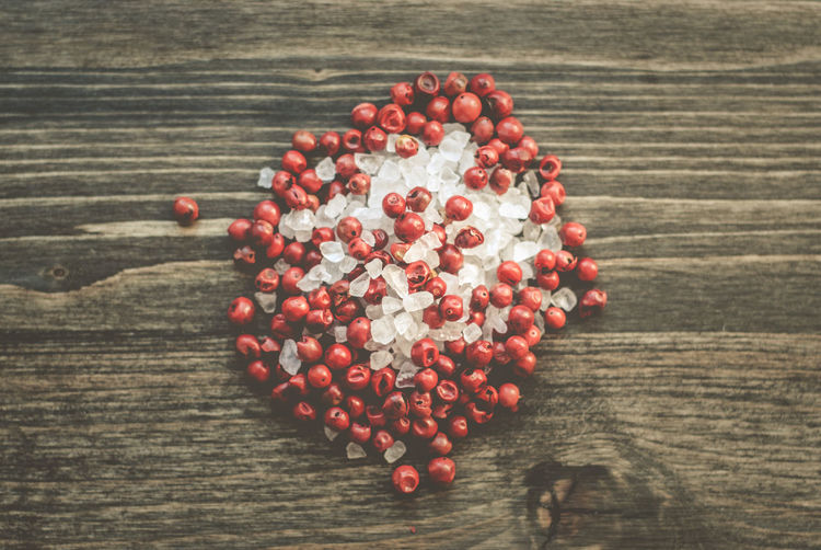 Directly above shot of pink peppercorns with sea salts on wooden table