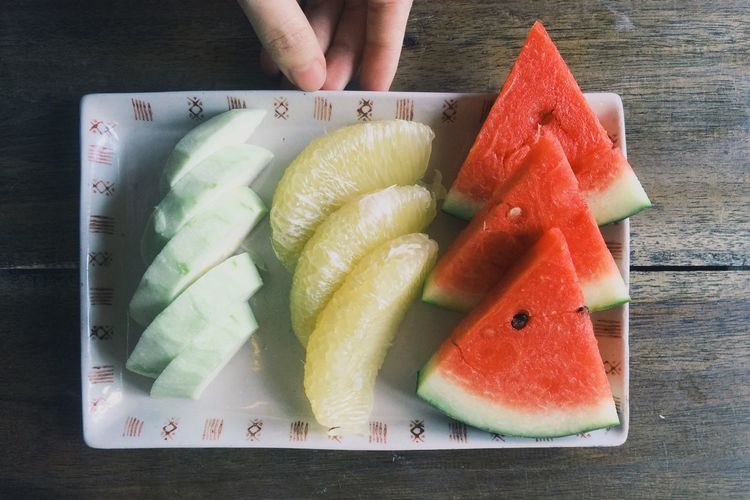 Cropped image of hand holding tray with fruits on table