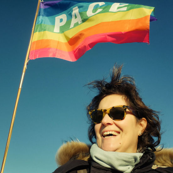 Smiling woman wearing sunglasses standing by rainbow flag against clear sky