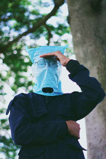 Low angle view of man wearing plastic bag while standing against tree