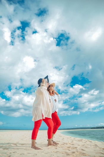 Rear view of woman standing at beach against sky