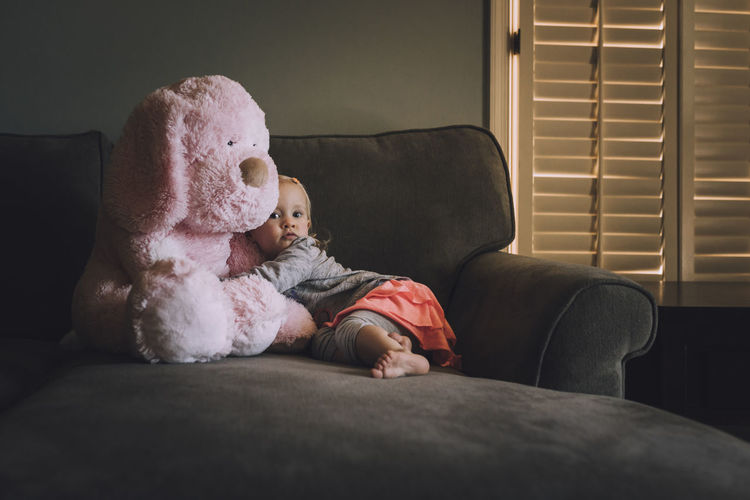 Portrait of girl with teddy bear on sofa at home