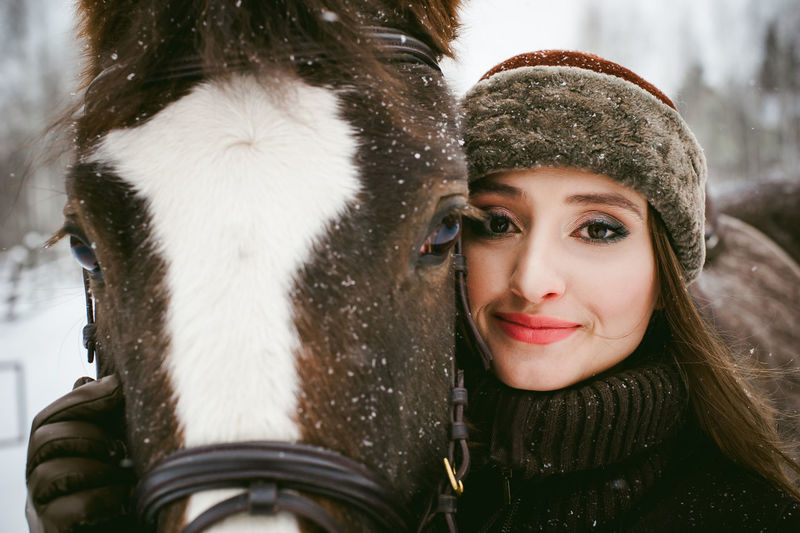 Close-up portrait of beautiful woman with horse during snowfall