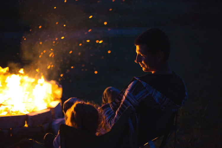 Dad and daughter sit at night by the fire in the open air in the summer in nature. family camping 