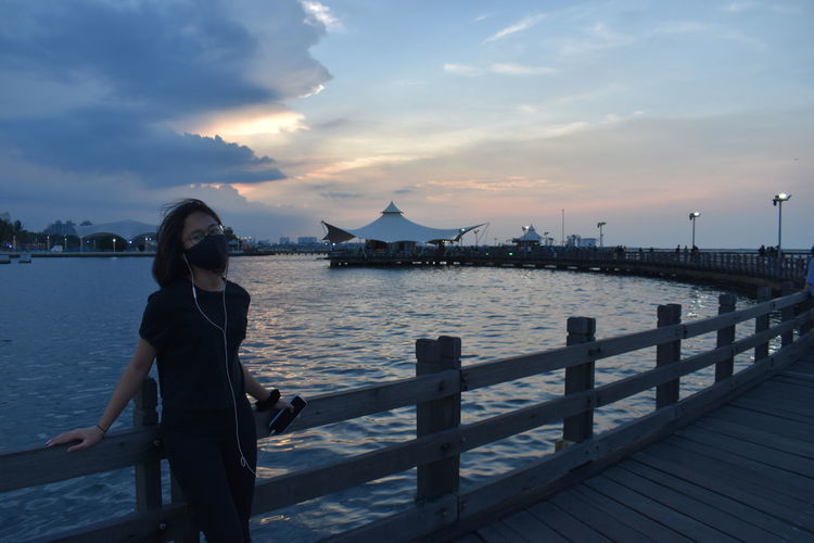 Man standing on pier over sea against sky during sunset