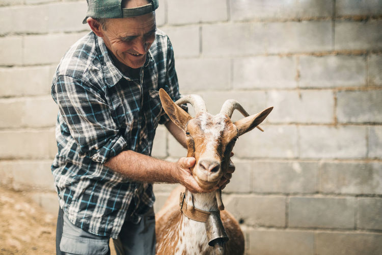 Male goat herder smiling while looking at goat in front of wall