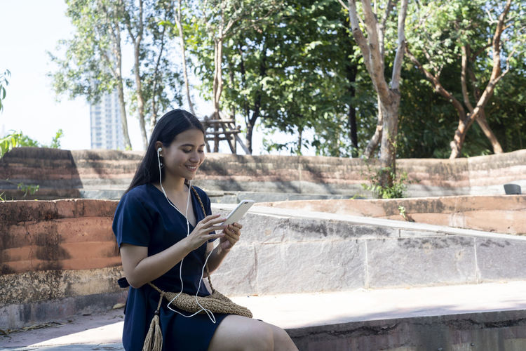 Young woman using phone while sitting on tree