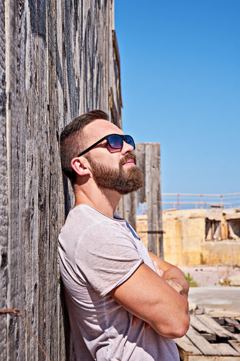 Bearded caucasian man in sunglasses stay near wooden wall outdoor