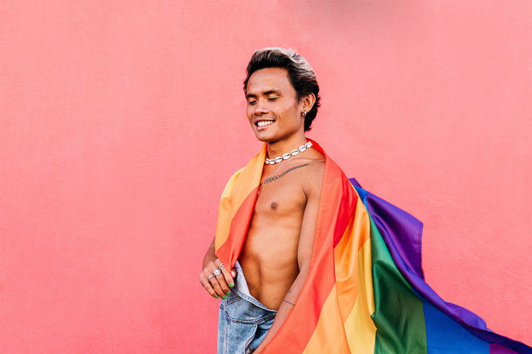 Gay man with multi colored flag against pink wall