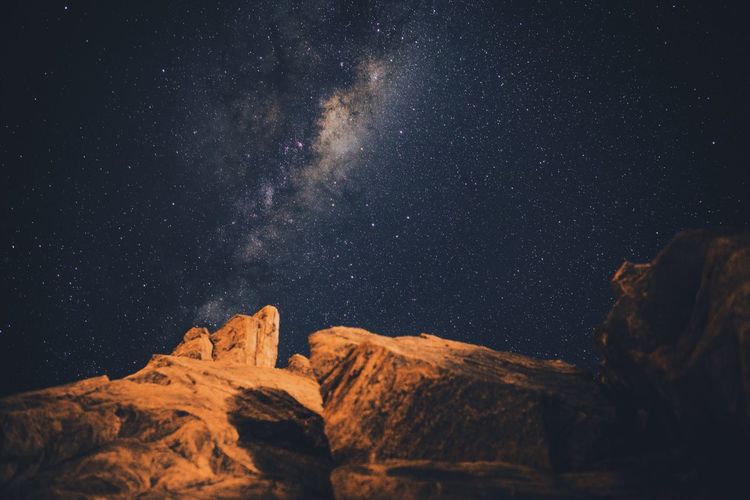 Low angle view of rocks against sky with star field