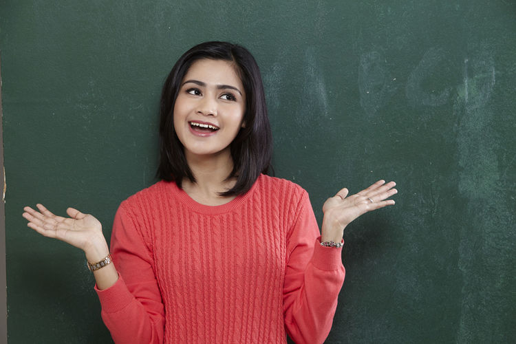 Cheerful female teacher gesturing while standing by blackboard