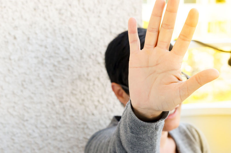 Close-up of person covering face with hand against wall