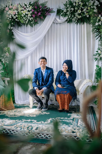Full length of smiling couple sitting on sofa in wedding ceremony
