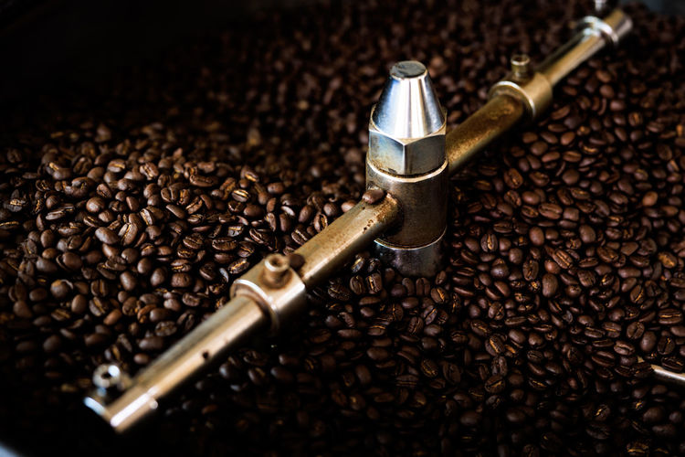 Fresh coffee beans and roasted spinning cover professional machine close up photo blur and dark 