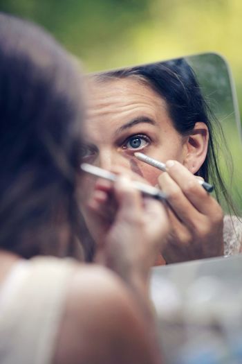 Reflection of woman applying eyeliner on mirror
