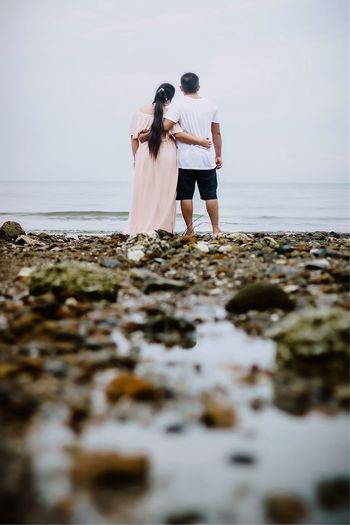 Rear view of woman standing on beach against sky