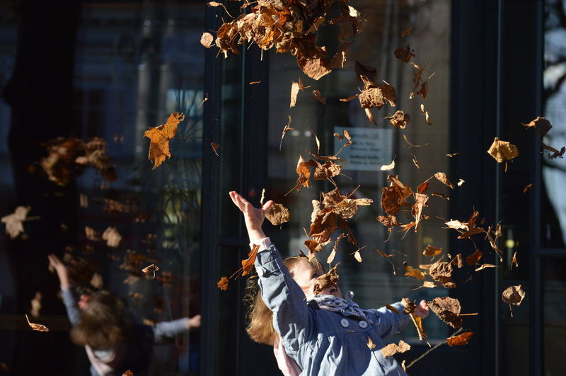 Girl throwing dry leaves in mid-air at city