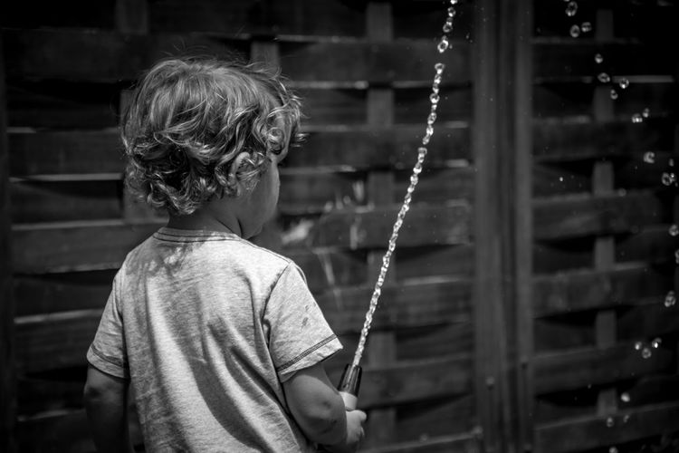 Rear view of boy spraying water outdoors