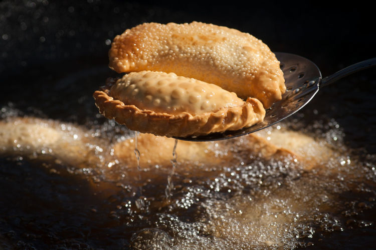 Close-up of fried empanada on ladle over pan