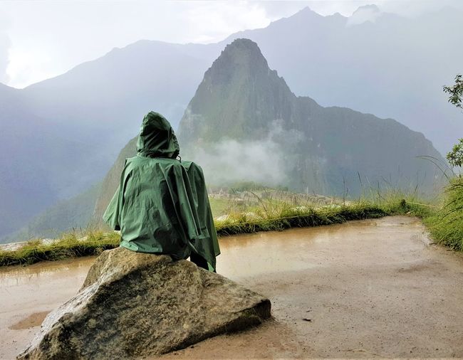 Rear view of person in raincoat sitting on rock at machu picchu