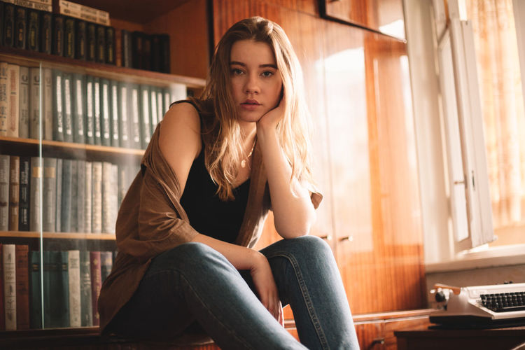 Young woman sitting by bookshelf