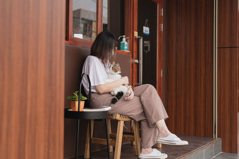Asian woman wearing protective mask sit and play with her cat at outdoor coffee shop