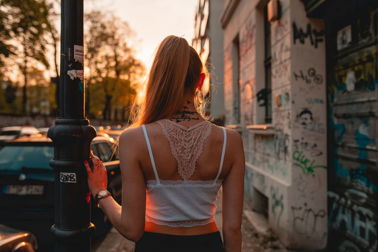 Rear view of young woman while standing on sidewalk during sunset