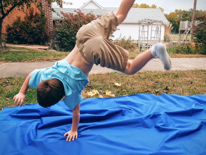 Full length of boy performing handstand on blue fabric in yard