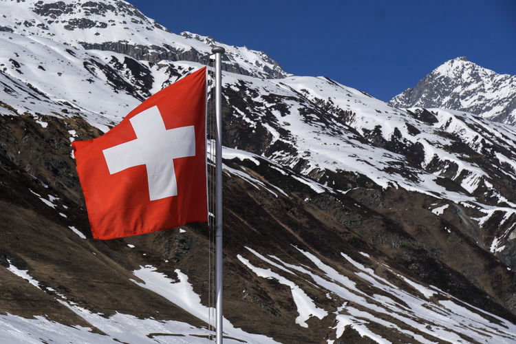Scenic view of swiss flag in front of snowcapped mountains against sky