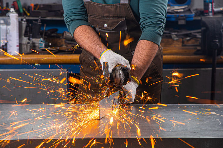 . a young male welder grinds a metal product with angle grinder in the garage
