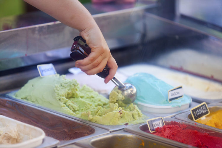 Close up on the hand of a young woman scooping an ice cream in gelato cafe.