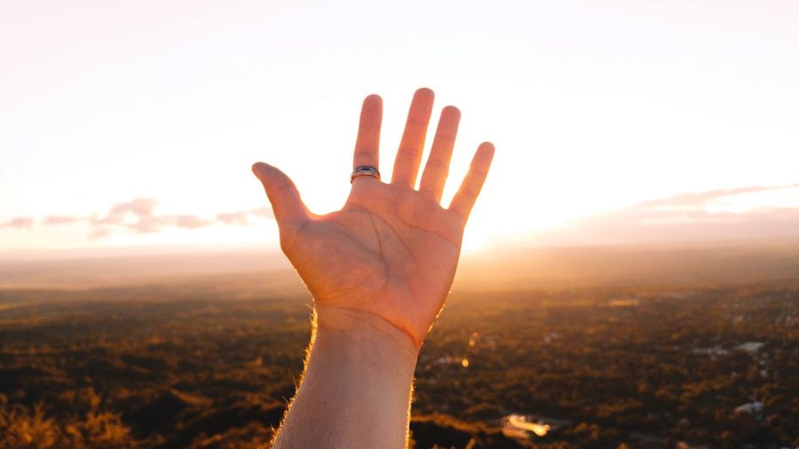 Cropped hand of man reaching sky during sunset