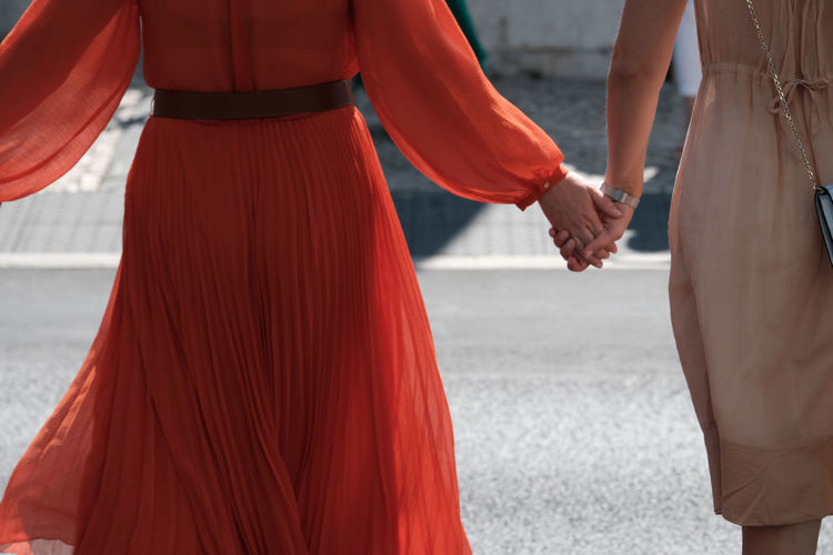 Midsection of friends holding hands while standing in city