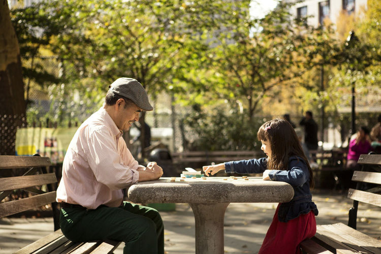 Grandfather and granddaughter playing board game while sitting at table in park