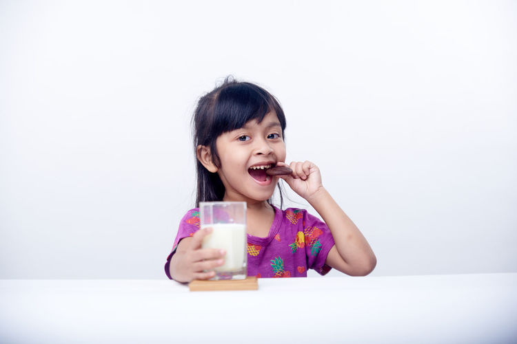 Portrait of young woman drinking milk against white background