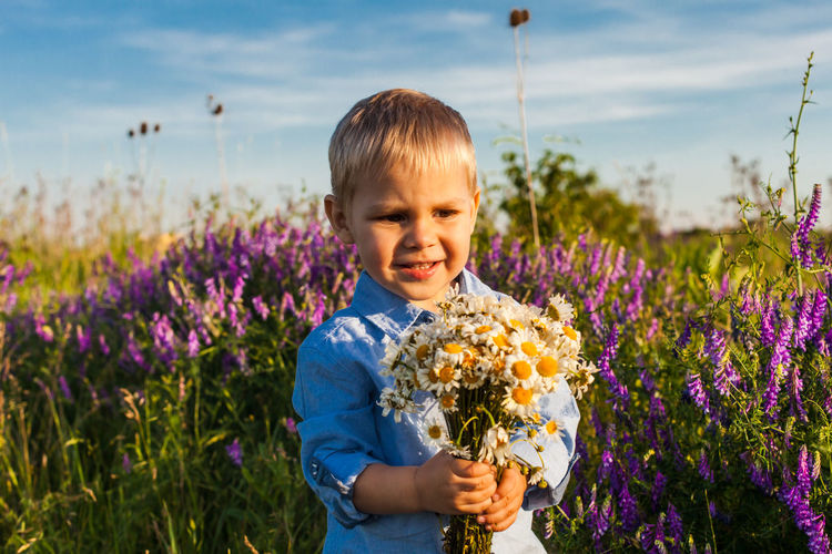Cute boy holding bouquet while standing on field