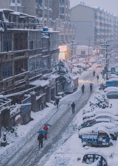 People on snow covered street against buildings in city