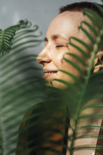 Smiling female entrepreneur with eyes closed by green leaves