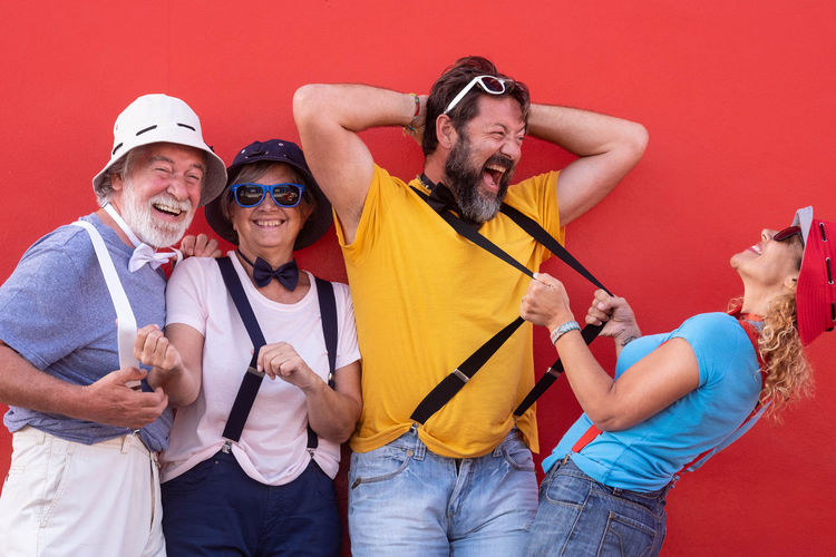 Cheerful family in suspenders standing against red wall