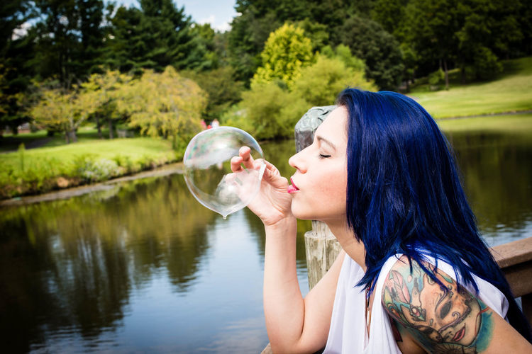 Side view of woman bowing bubble by lake