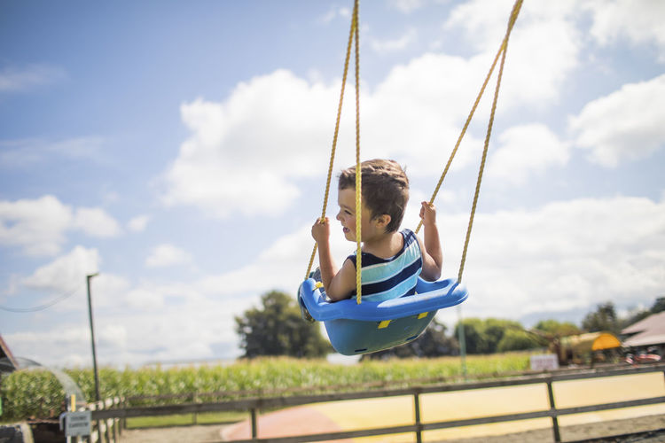 Man sitting on swing at playground against sky
