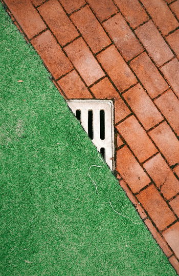 View of a drain in between brick and grass
