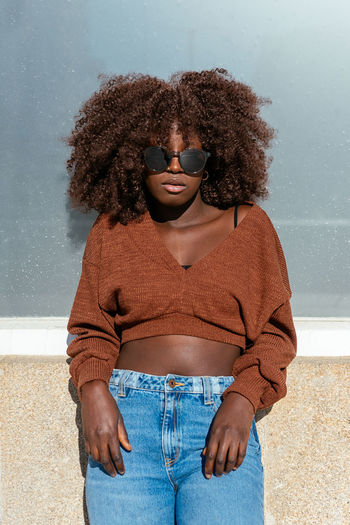 Young woman wearing sunglasses while standing against wall