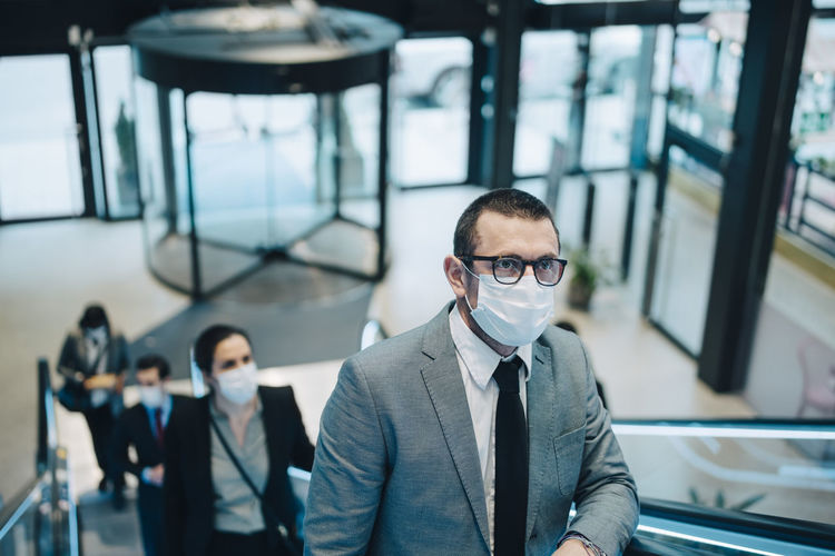 Business people moving upwards on escalator during pandemic