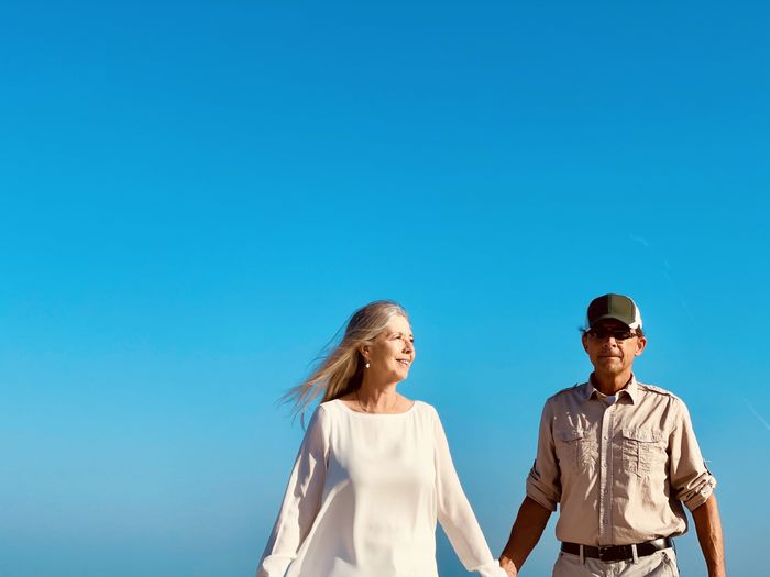 Active senior couple holding hands as they walk together against blue sky. waist up and copy space.  