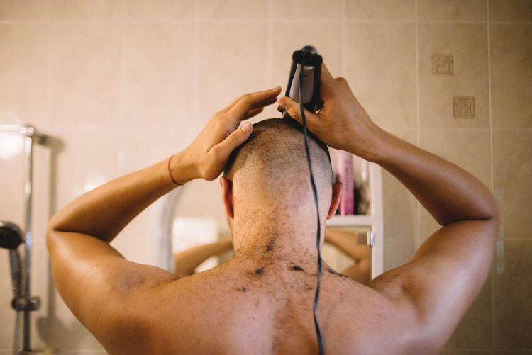 Rear view of man shaving head in bathroom