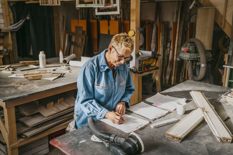 Female senior entrepreneur preparing document over workbench at repair shop