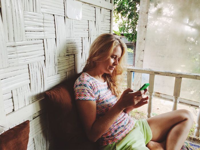 Woman using smart phone while sitting at porch