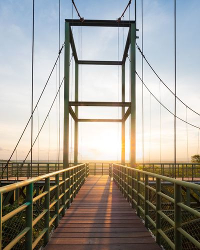 Footbridge against sky at sunset